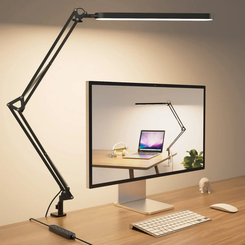 Adjustable clamp arm LED desk lamp in black mounted on wooden desk beside computer monitor