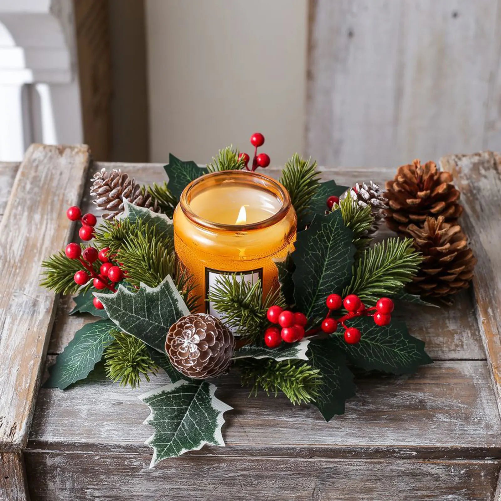 Festive holiday candle ring centerpiece with pine needles, pinecones, holly leaves, and red berries around an amber jar candle