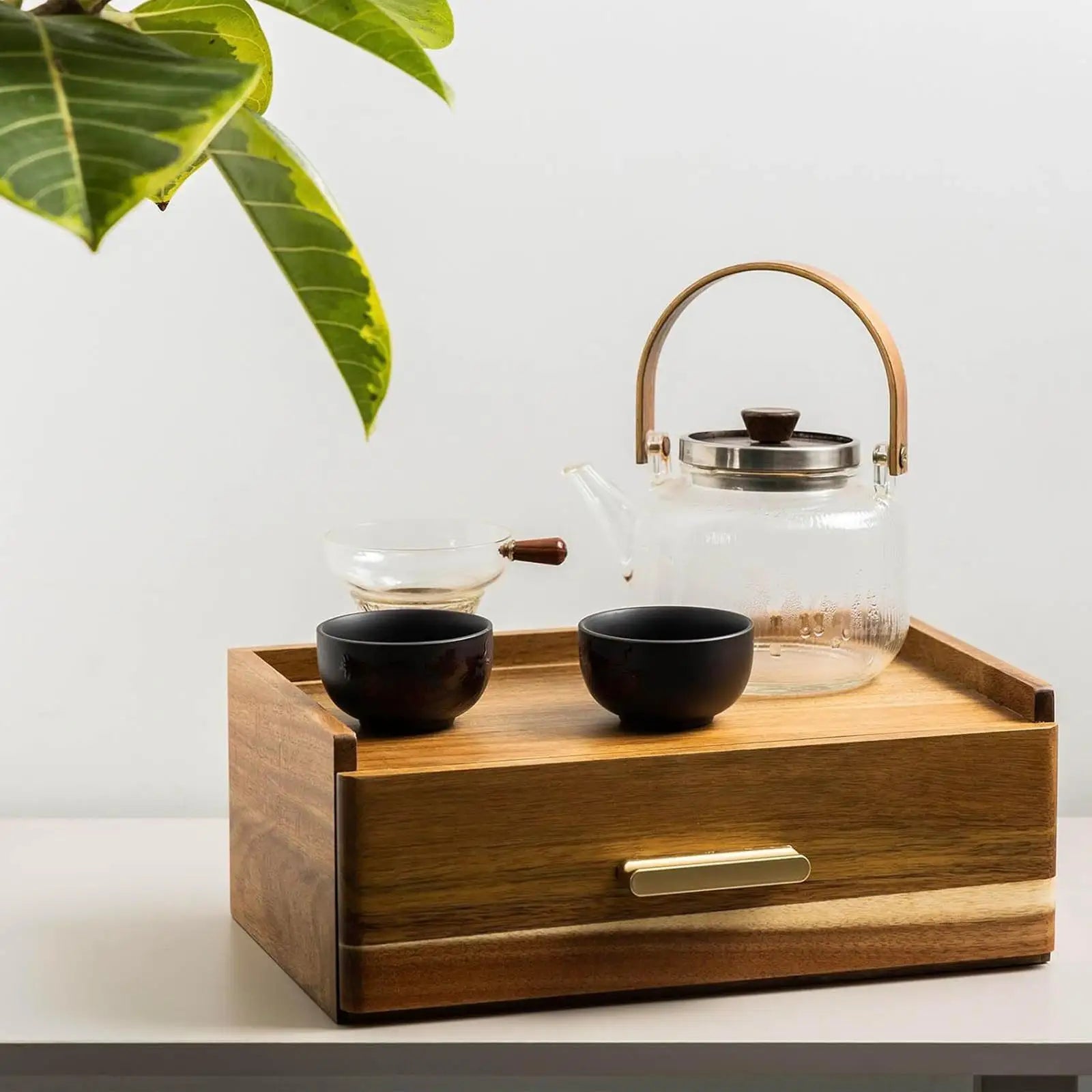 Wood tea bag organizer box with glass tea set on top, placed on a white table