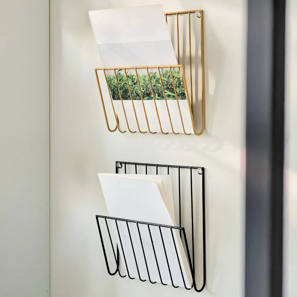 Close view of gold and black wall-mounted racks on a white wall, papers inside