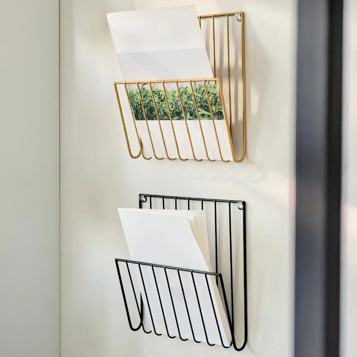 Close view of gold and black wall-mounted racks on a white wall, papers inside