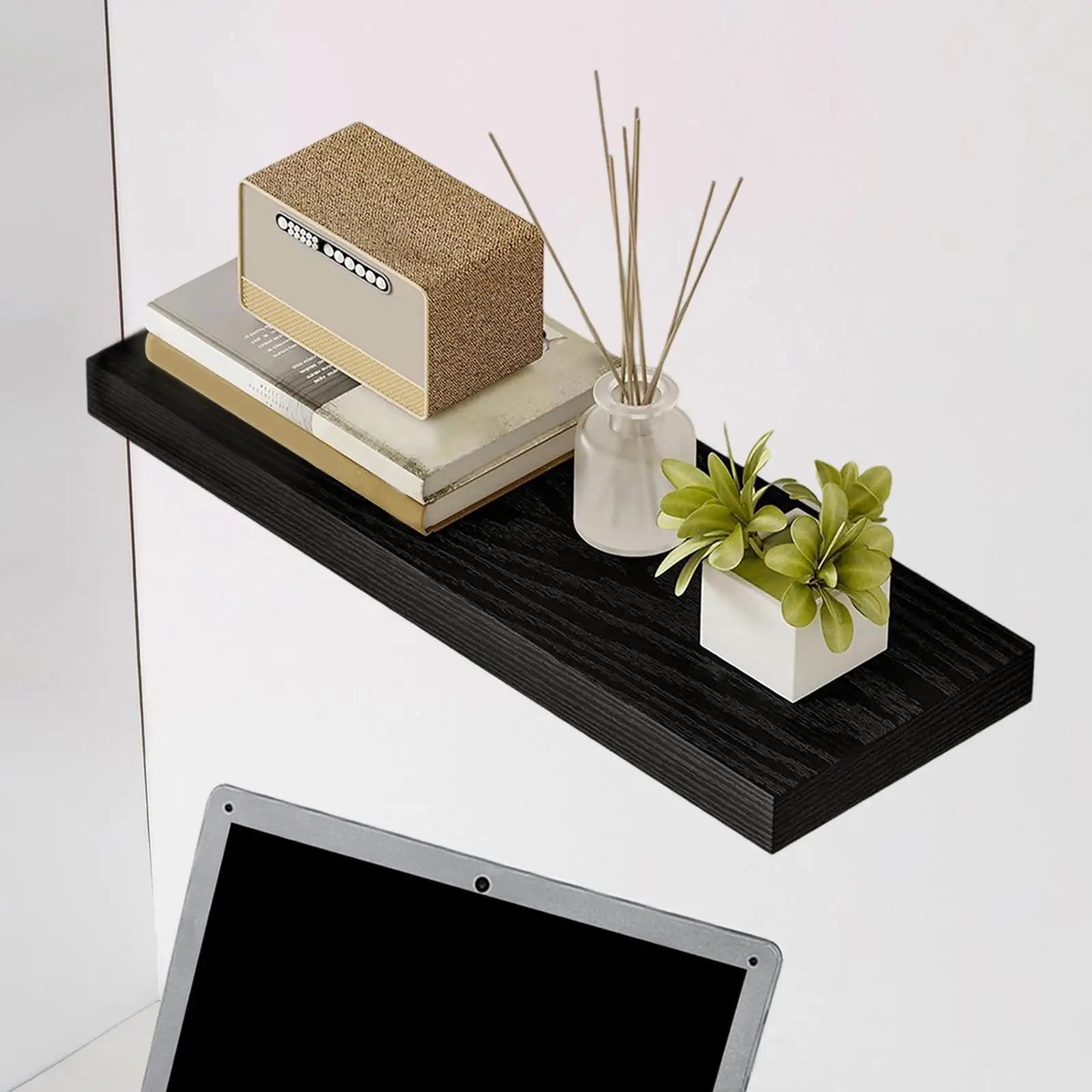 Black wood floating shelf mounted on a wall, styled with books, a small radio, a glass jar, and a plant
