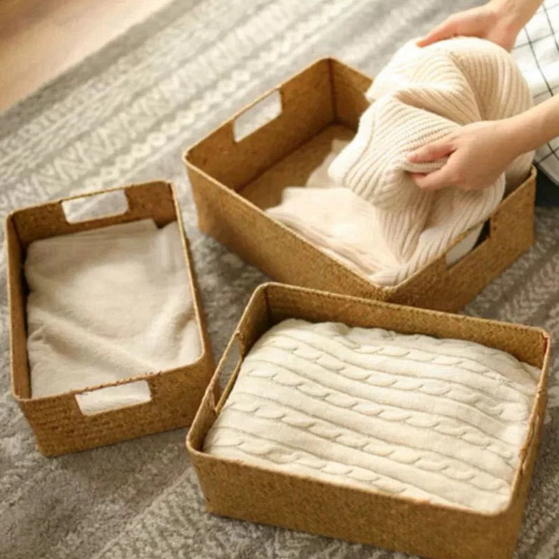 Hands placing cozily folded knitwear in seagrass baskets on soft rug