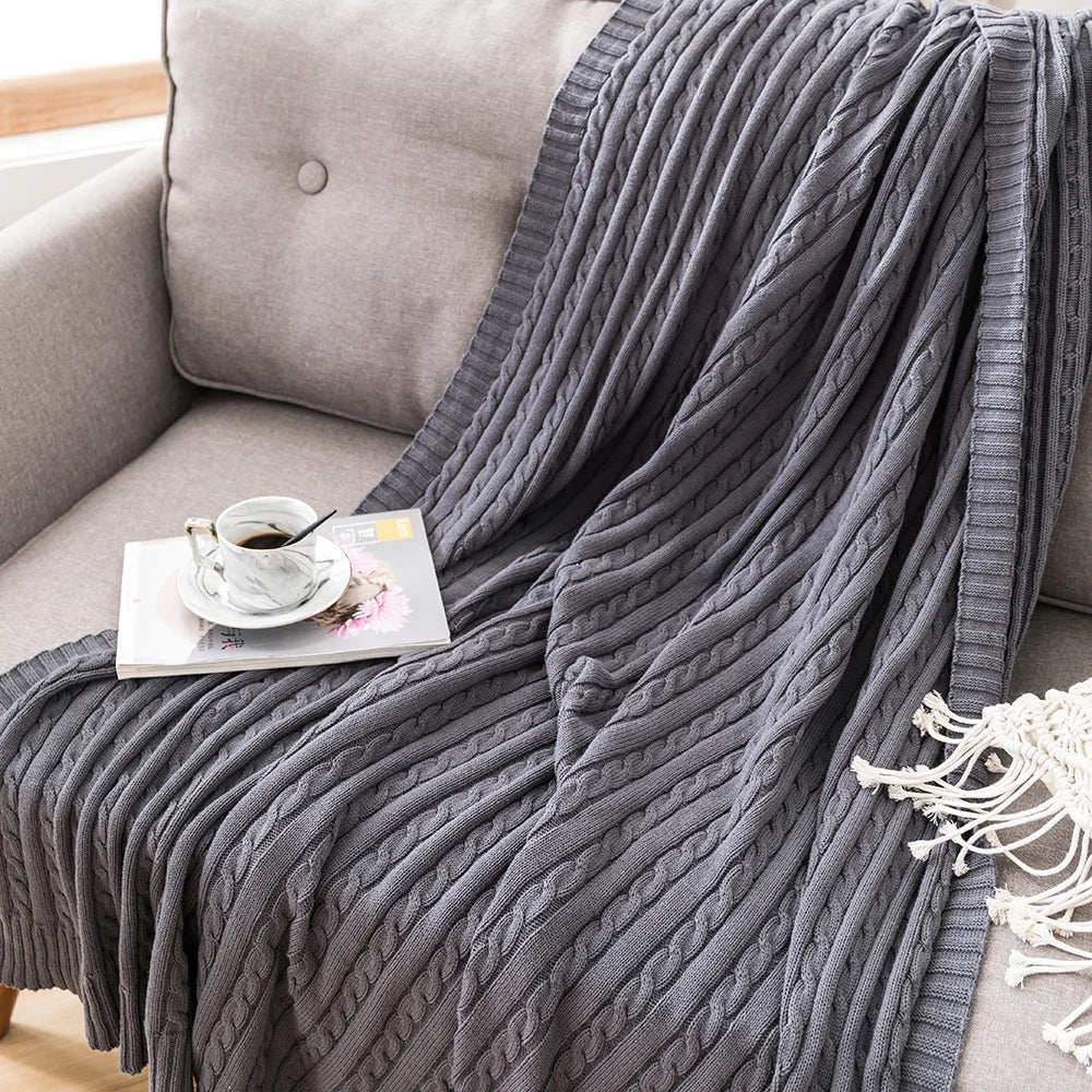 close-up of dark grey cable knit cotton throw on a sofa with a cup and magazine