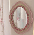 Pink baroque oval wall mirror with rose trim hung in a softly lit bedroom setting