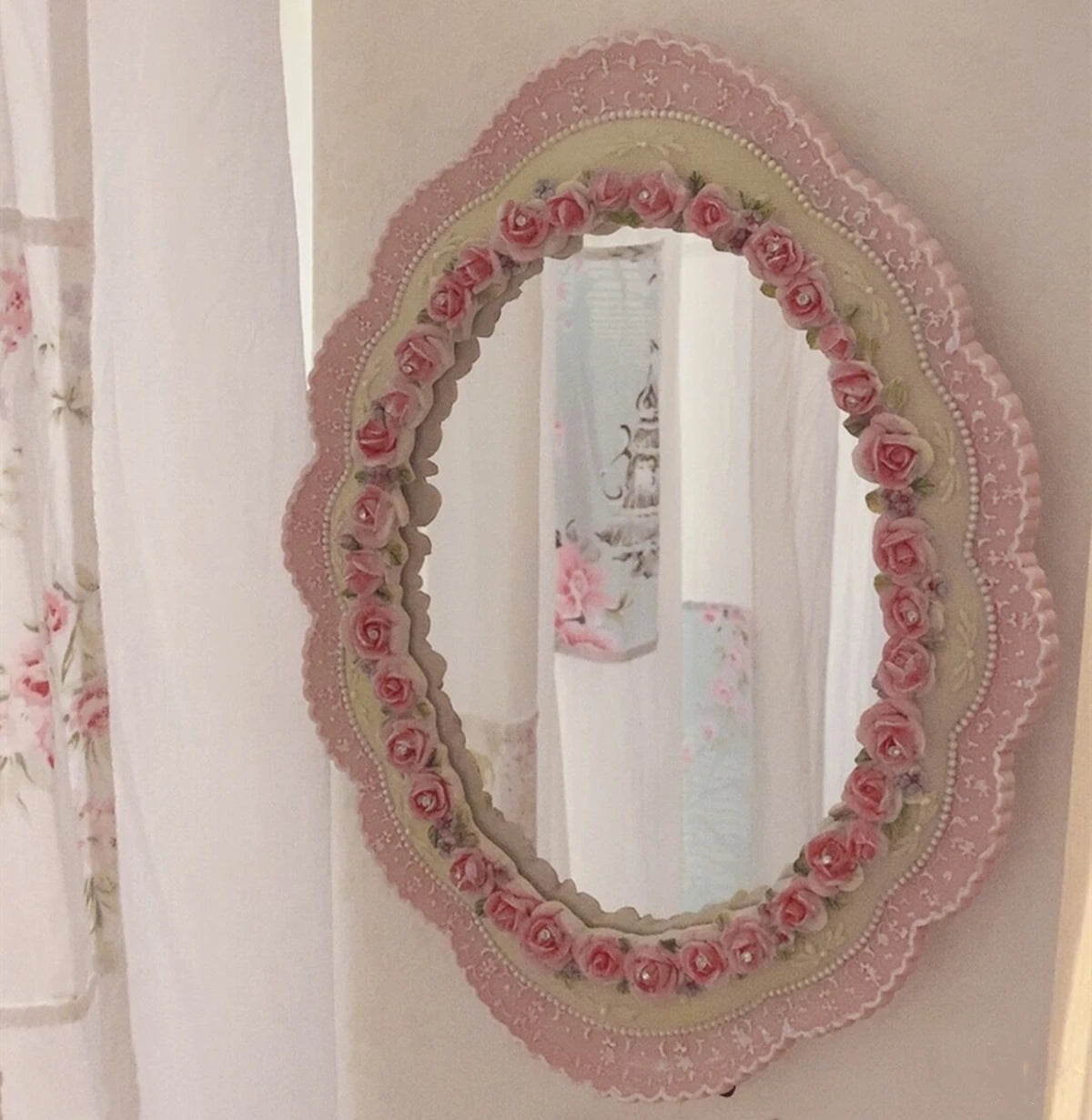 Pink baroque oval wall mirror with rose trim hung in a softly lit bedroom setting