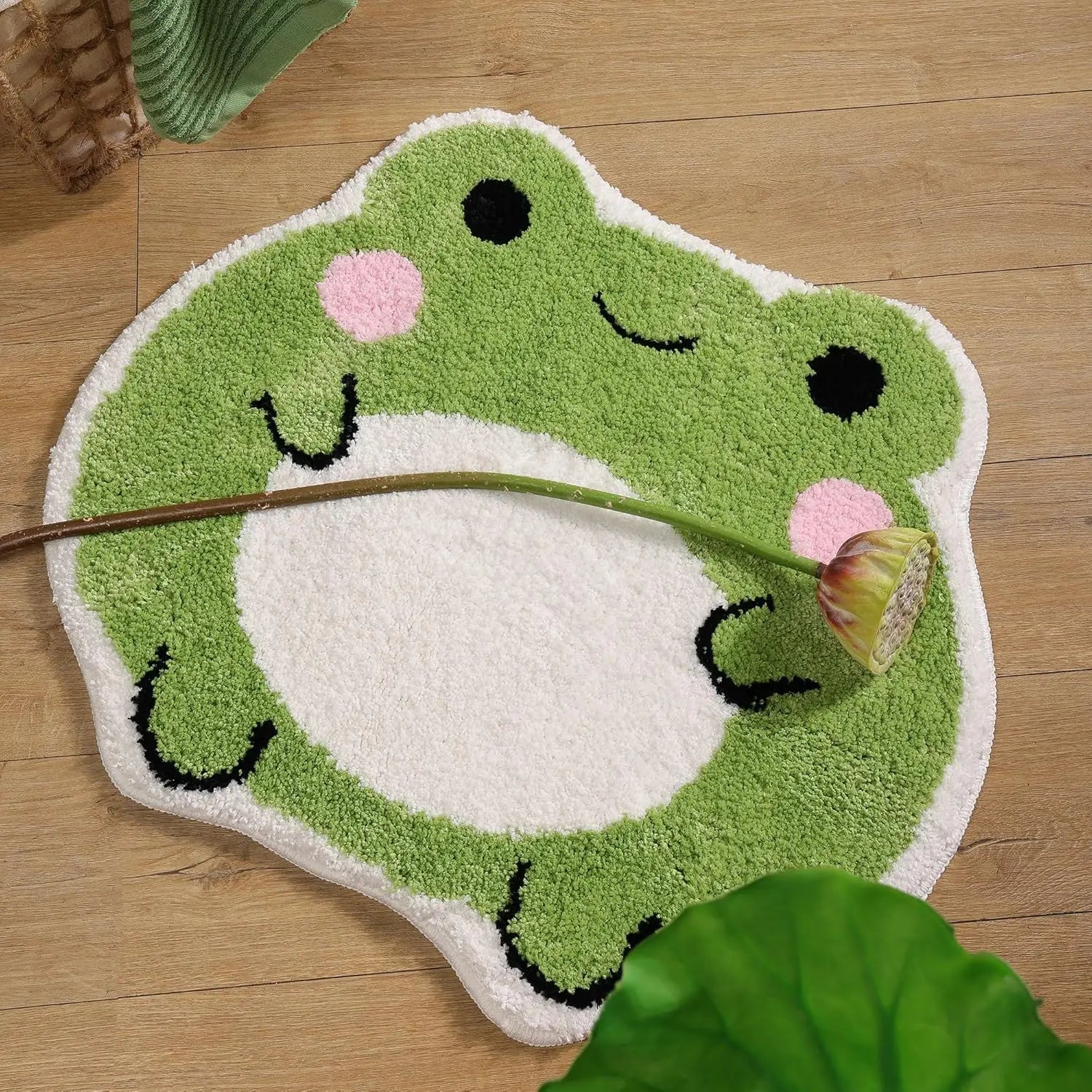 Frog bath rug resting on a wood floor with a flower stem, closeup of round belly and blushing cheeks
