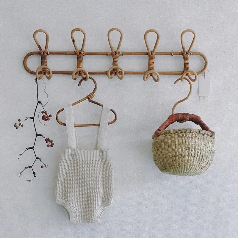 Five-hook rattan wall rack holding a child's romper and woven basket on a nursery wall