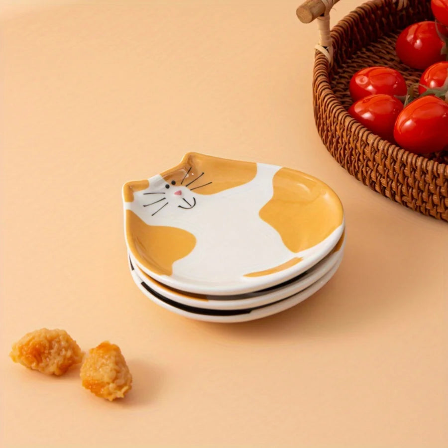 Stack of ceramic cat spoon rests in orange and black color on a kitchen counter next to a basket of tomatoes