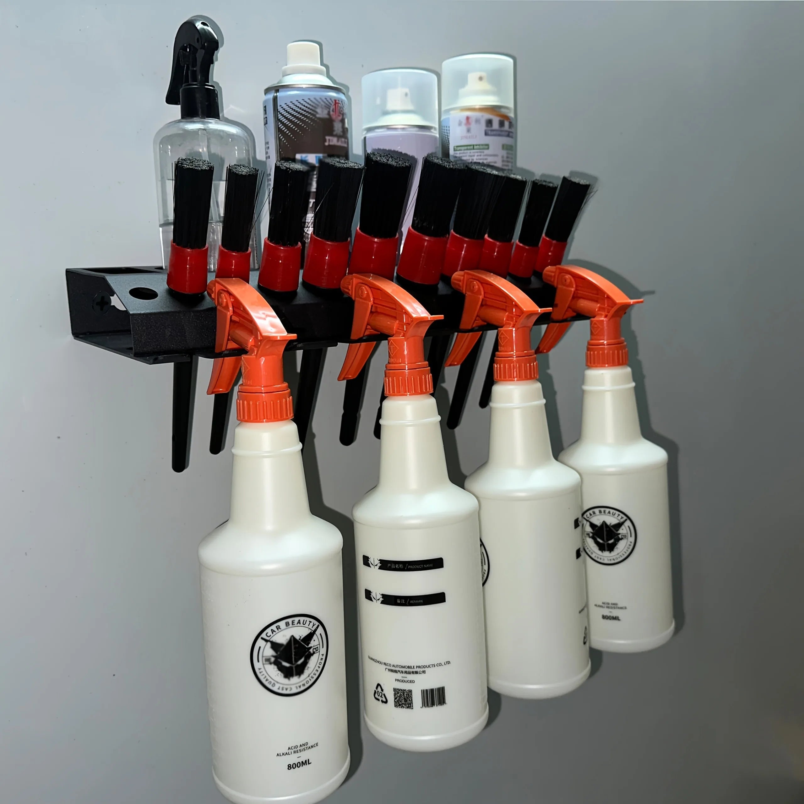 Wall-mounted spray bottle organizer in a garage with multiple bottles and brushes