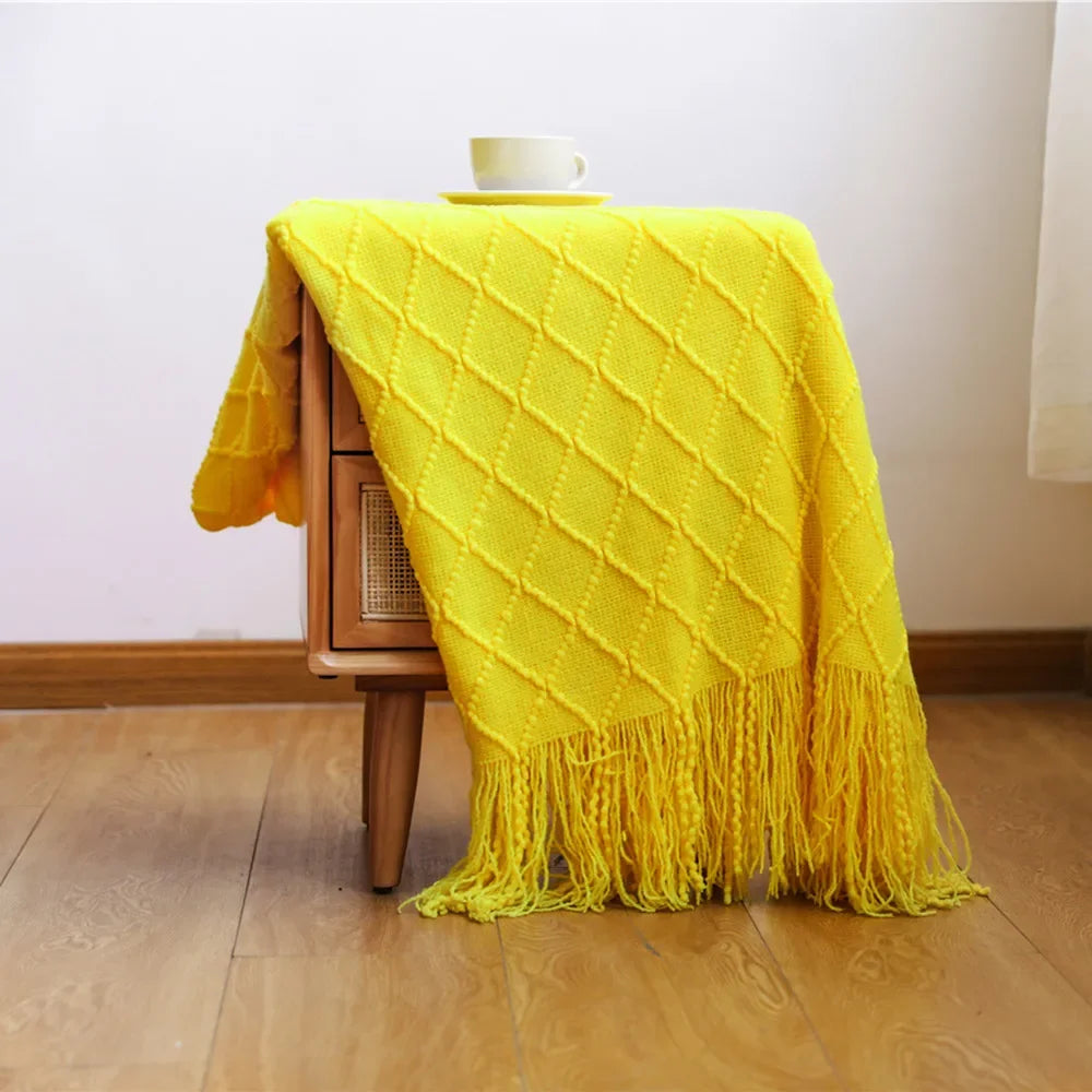 Yellow knit throw blanket with tassels on a wooden table