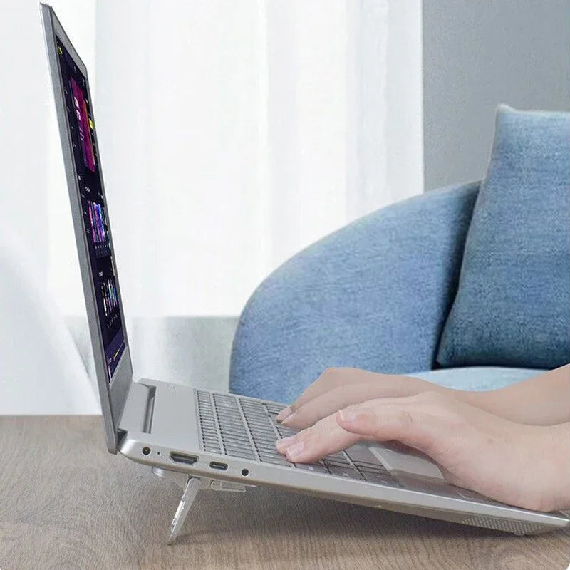 Laptop raised on mini foldable risers on a table with a person typing, blue sofa in background