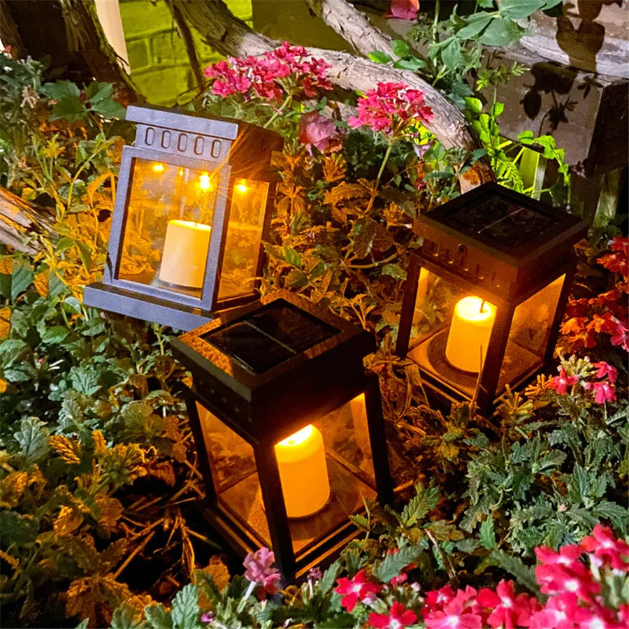 Three solar candle lanterns glowing among garden flowers at night
