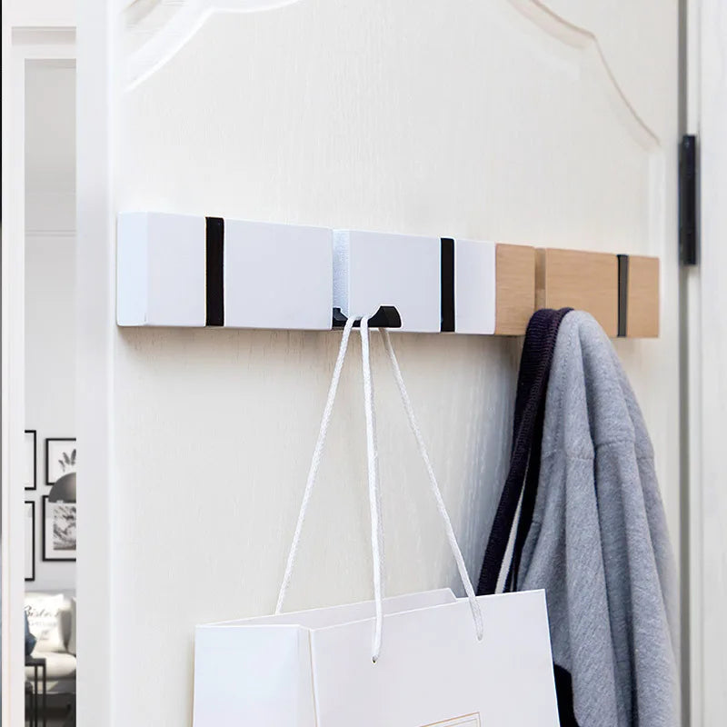 White wooden foldable hook rack mounted on the back of a door, holding a bag and a gray garment