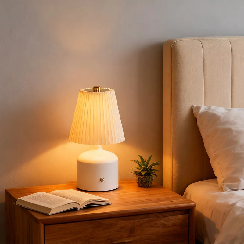 White pleated table lamp on a wooden nightstand with a warm glow