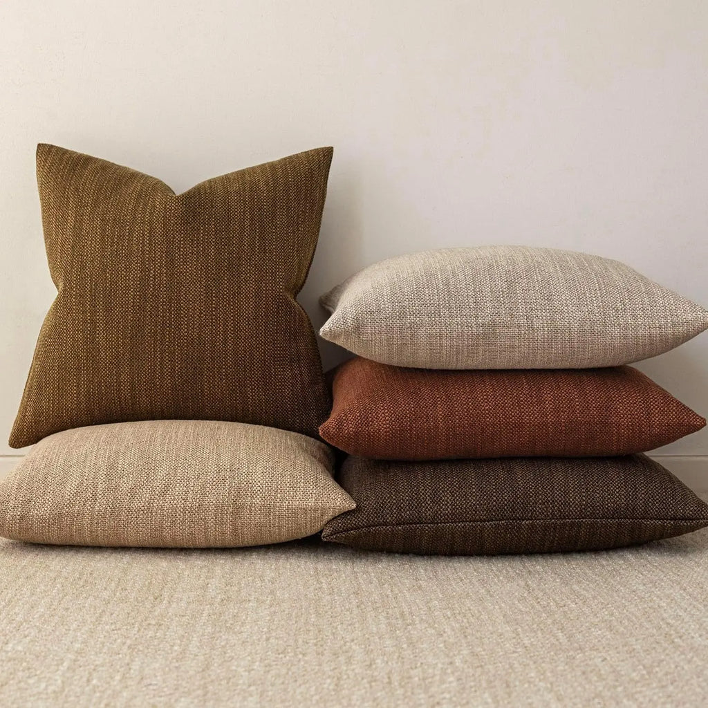Stack of woven chenille throw pillow covers in brown, cream, burnt orange, and coffee colors