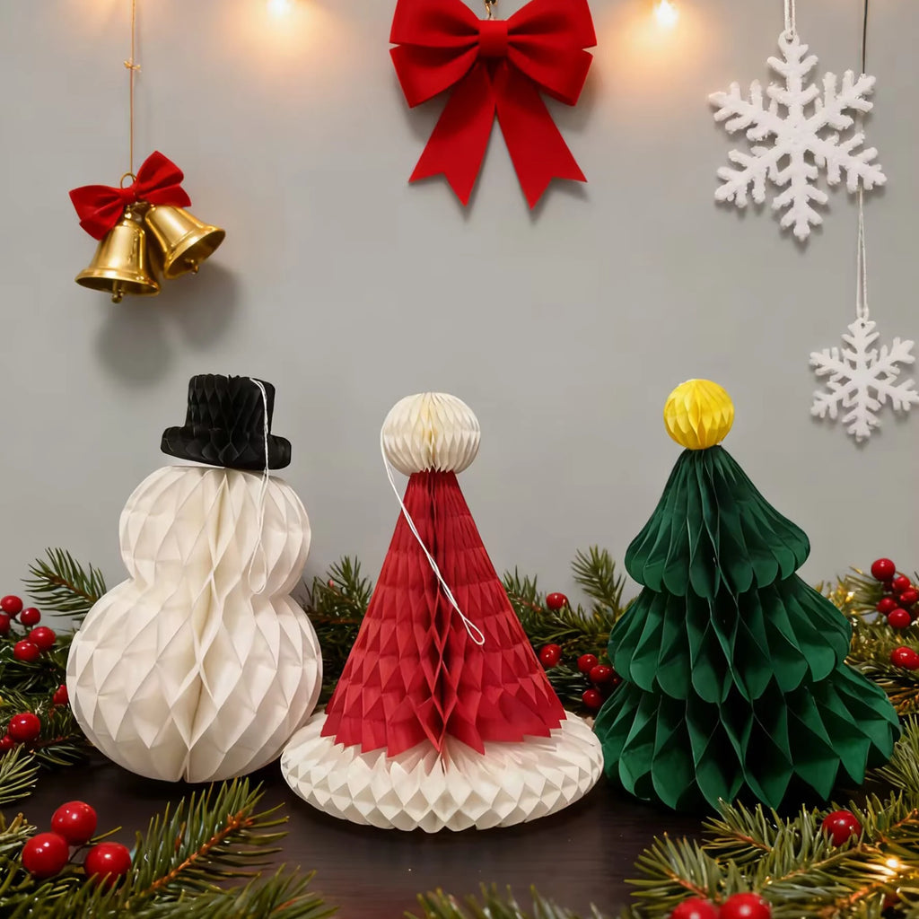 Set of three honeycomb paper Christmas decorations—snowman, Santa hat, and tree—on a holiday table with festive garland
