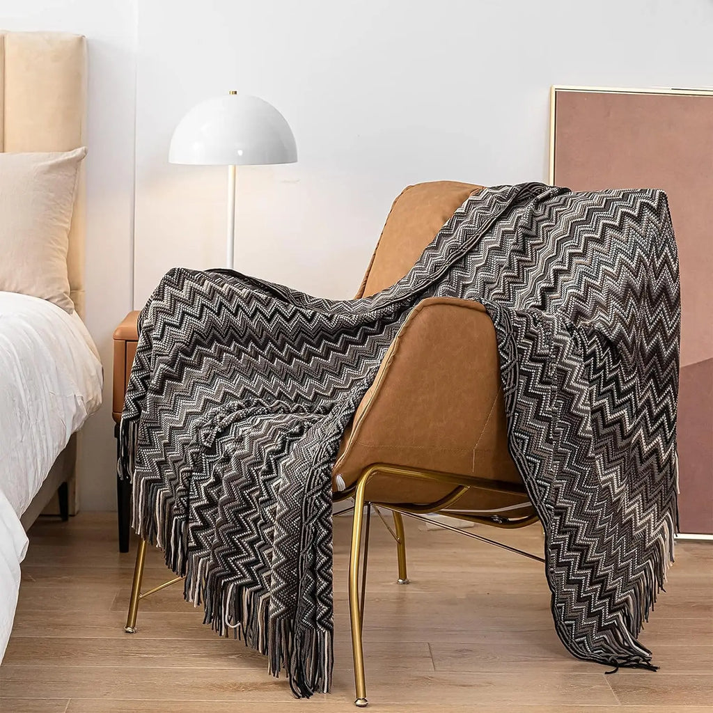 Monochrome black and white zigzag knit throw blanket with tassels spread over a leather accent chair beside a bed