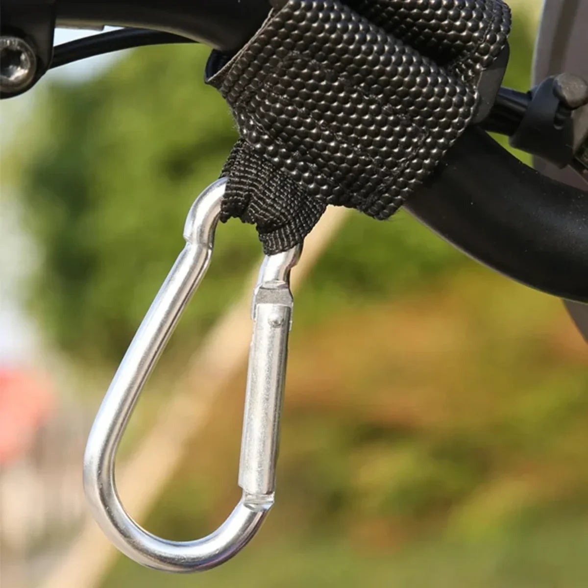 Silver carabiner handlebar locking hook attached to a bike handlebar using a black strap outdoors