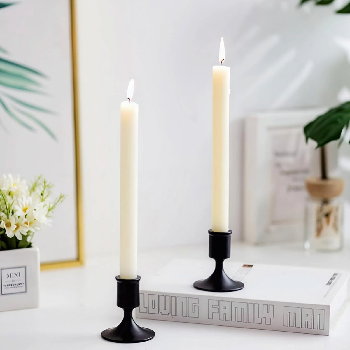 two black brushed metal taper candle holders with ivory candles, placed on a stack of books in a cozy living space