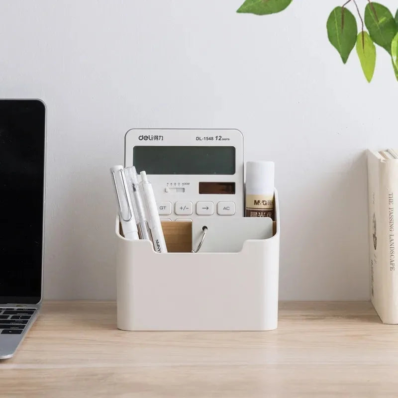 White compartment storage box holding desk supplies like pens and a calculator on a home office desk.