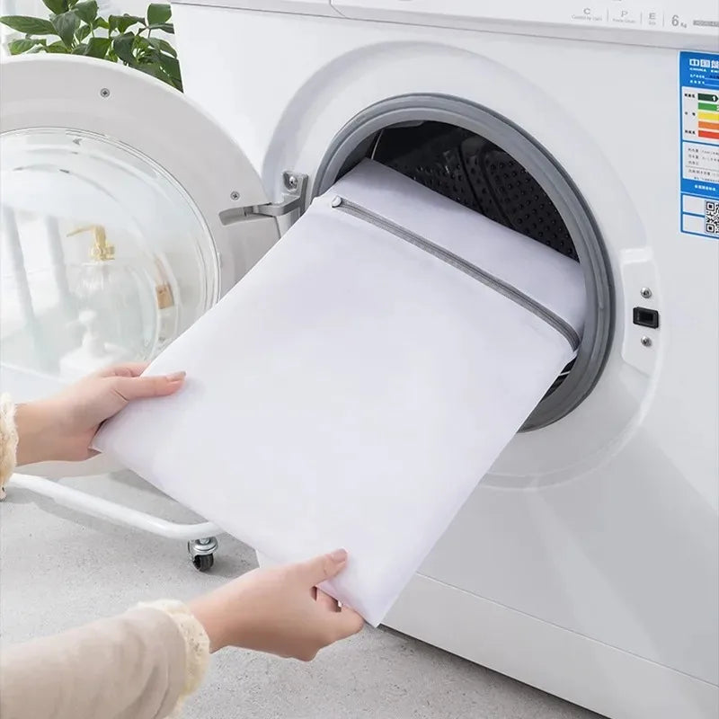Large white mesh laundry bag being placed into a front-loading washing machine
