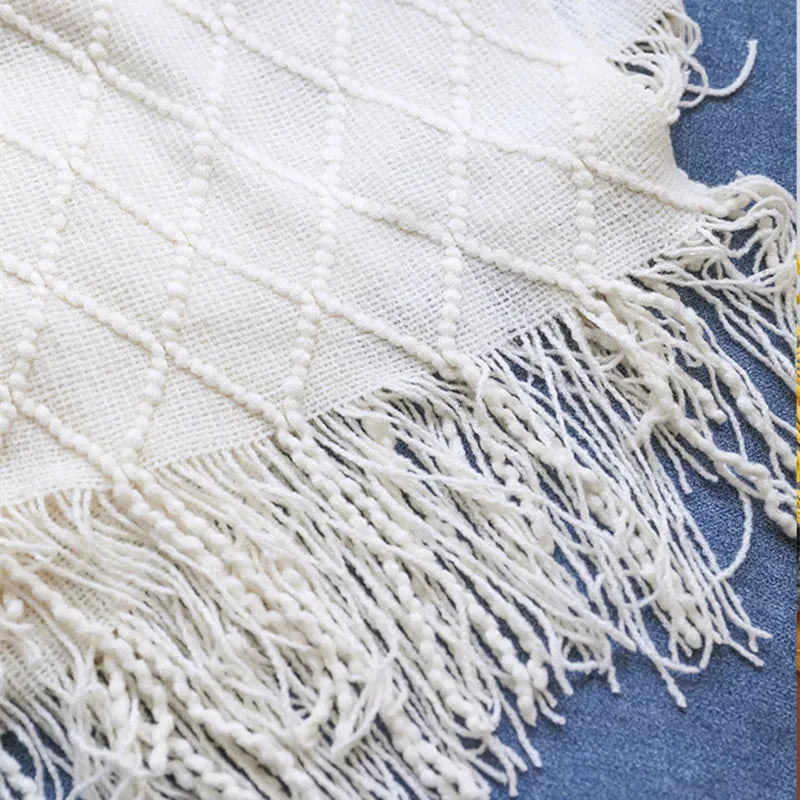 Close-up of off-white knit blanket with diamond pattern and tassel fringe