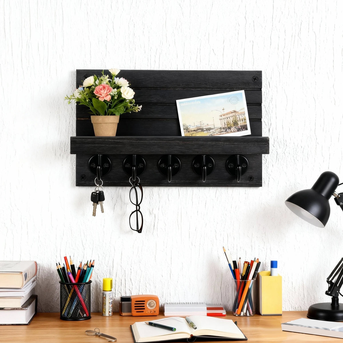 Black wooden key and mail holder with five hooks, shelf holding flowers and postcards, mounted above a home office desk.