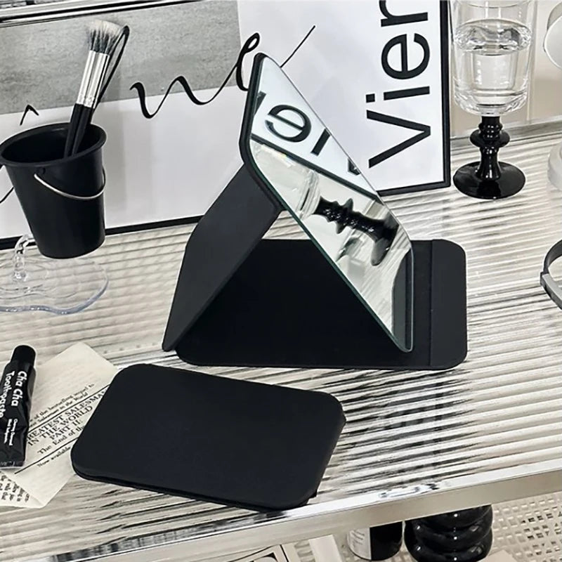 Foldable black PU leather makeup mirror in use, with cover shown flat next to mirror.
