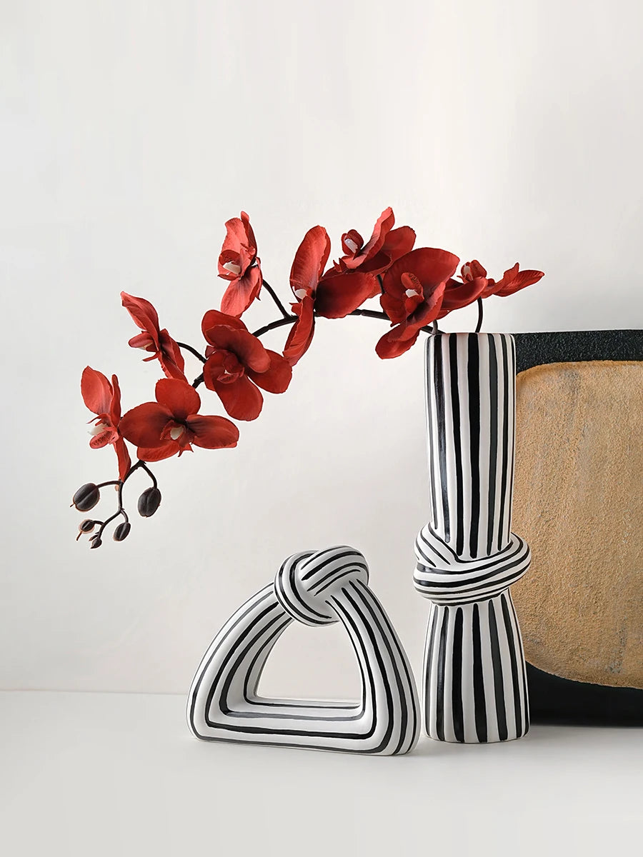 Set of black and white striped knot ceramic vases styled with vibrant red orchid stems on a minimalist white background.