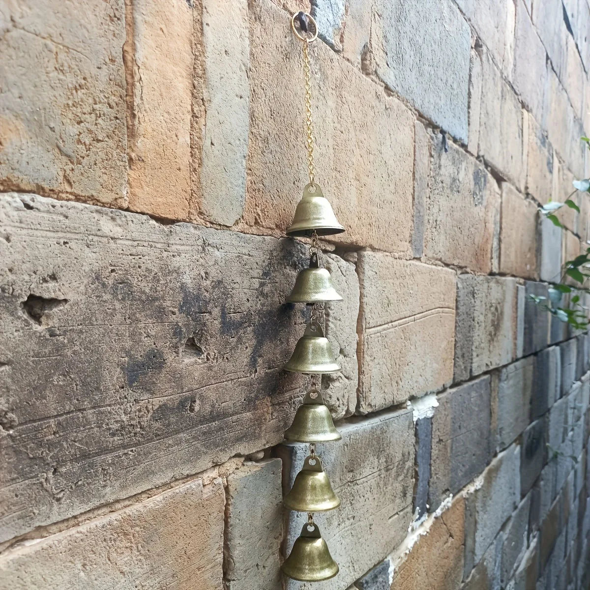 metal bell wind chime hanging on an outdoor brick wall