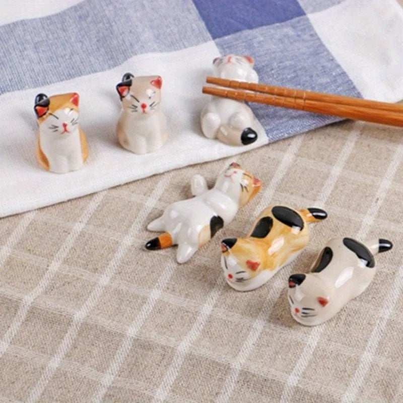 six ceramic cat-shaped utensil rests on a table with chopsticks
