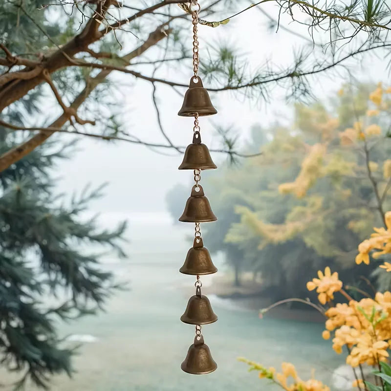 Handmade iron wind chime with six rustic bells hanging from a tree branch outdoors