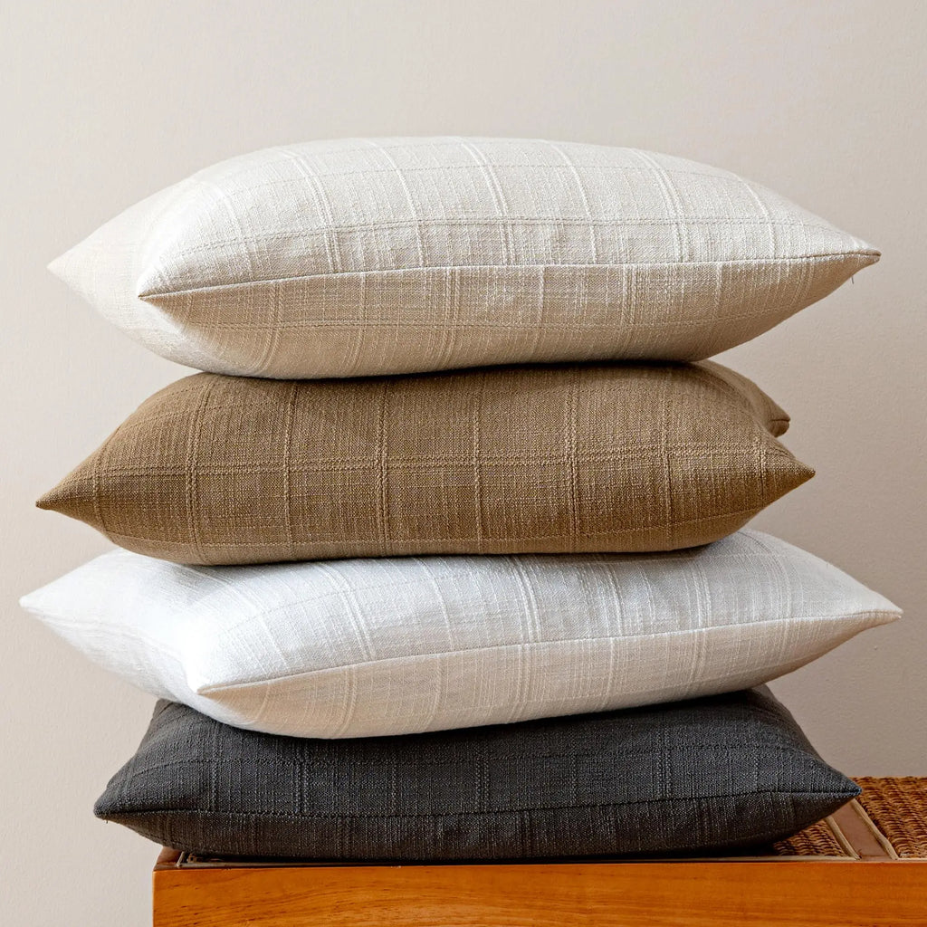 Stacked linen plaid pillow covers showing four neutral colorways on a wood side table