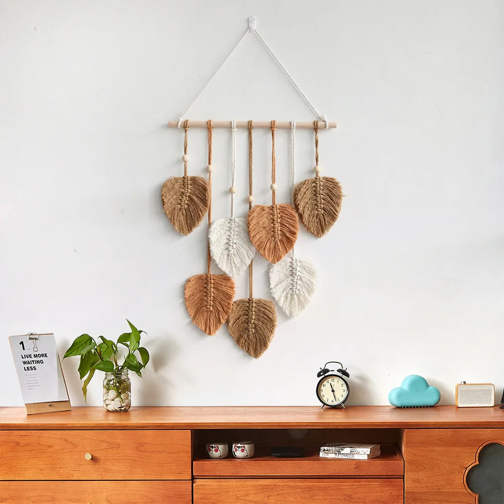 Khaki and cream woven leaf wall hanging on white wall above wooden cabinet