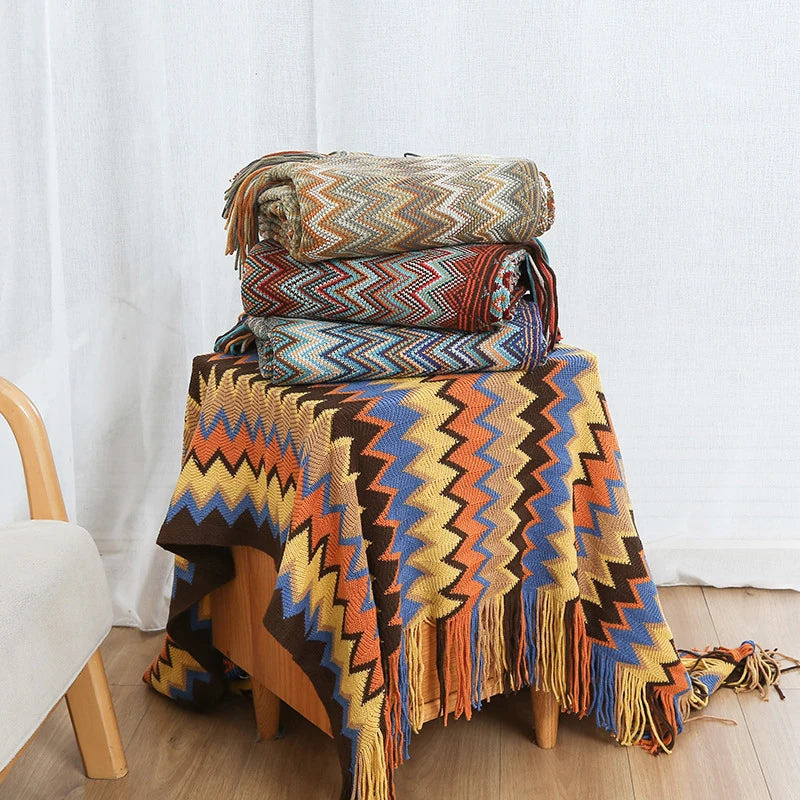 Colorful boho knit throw blankets with tassels folded and draped on a wooden chair in a cozy living room