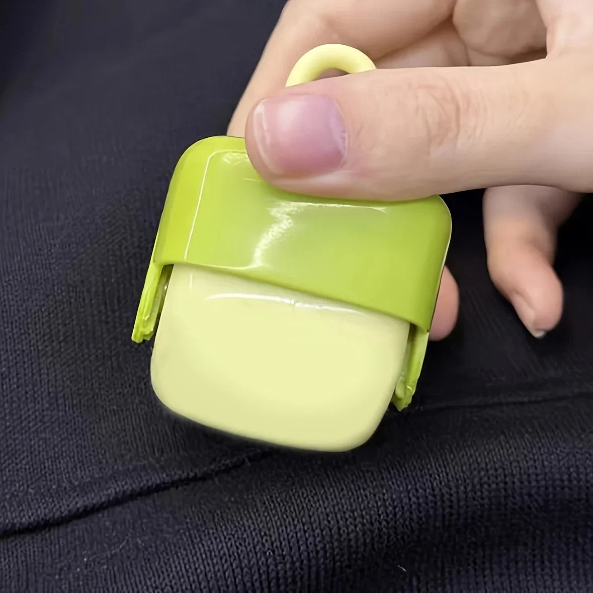 Portable lint roller in green and yellow being held against a dark fabric surface