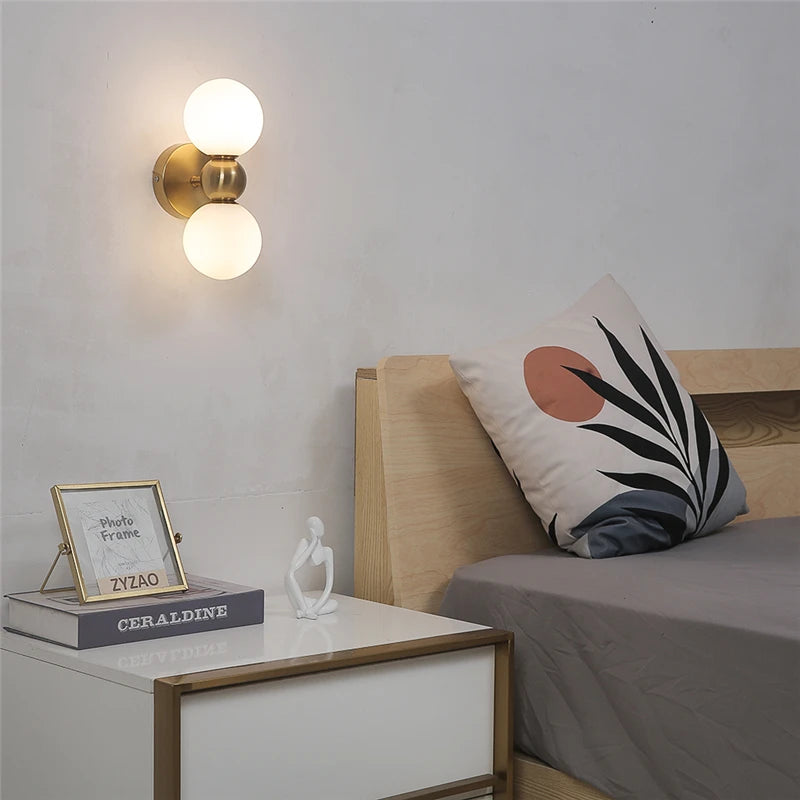Double globe wall sconce mounted above a modern bedroom nightstand with decorative art and pillow