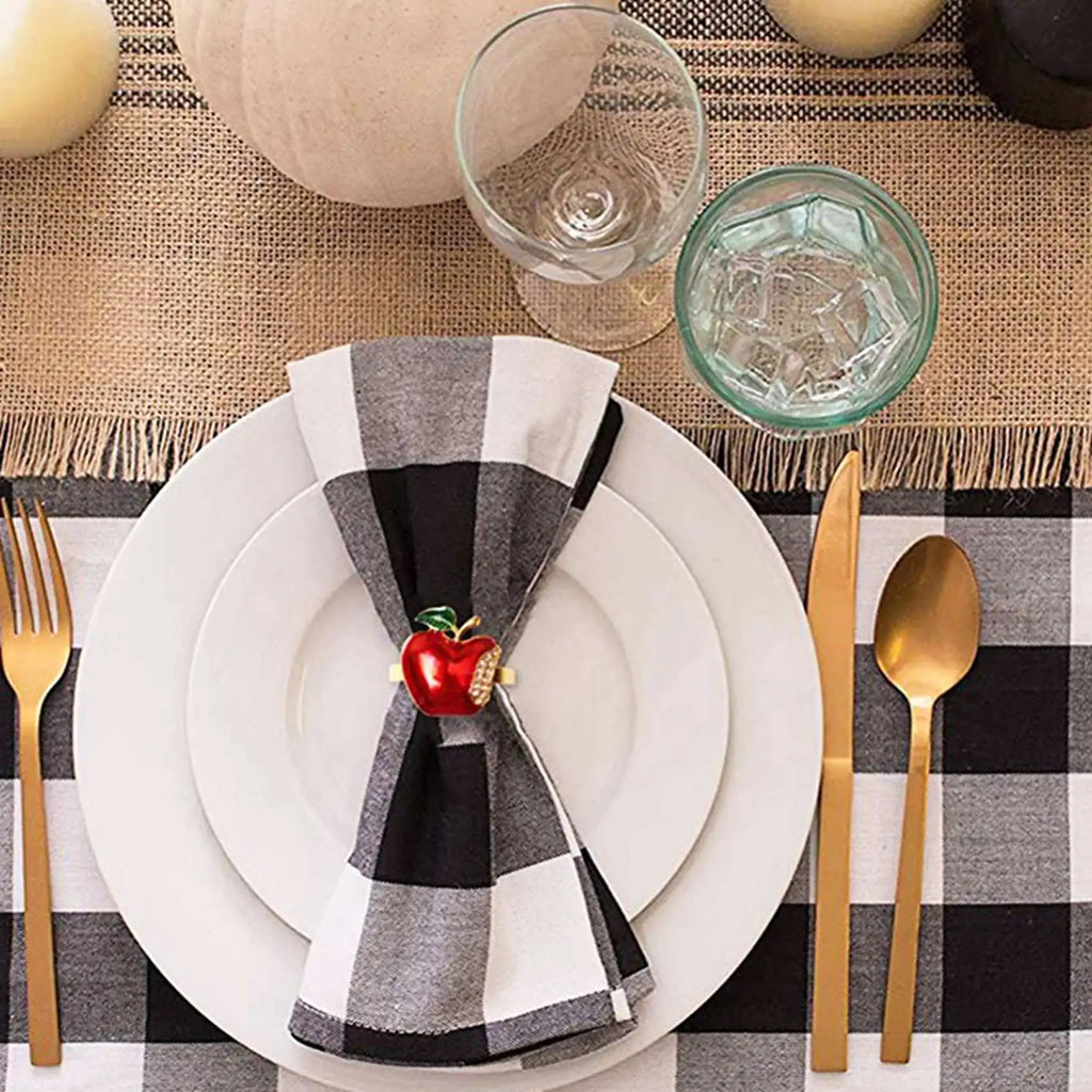 Apple napkin ring holding a black and white check napkin on a formal table setting with gold cutlery