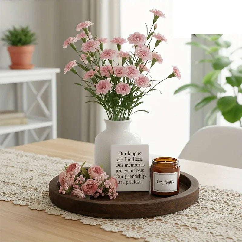 Dark wood round tray holding a vase with pink flowers, a small sign, and a candle on a dining table