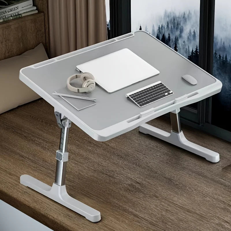 Adjustable gray lap desk set on a wood nook, holding a laptop, headphones, and keyboard