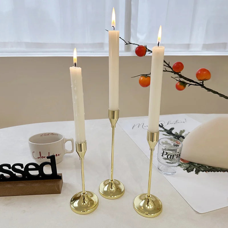 Gold metal candle holders set with lit taper candles displayed on a dining table, surrounded by mugs and decorative accents