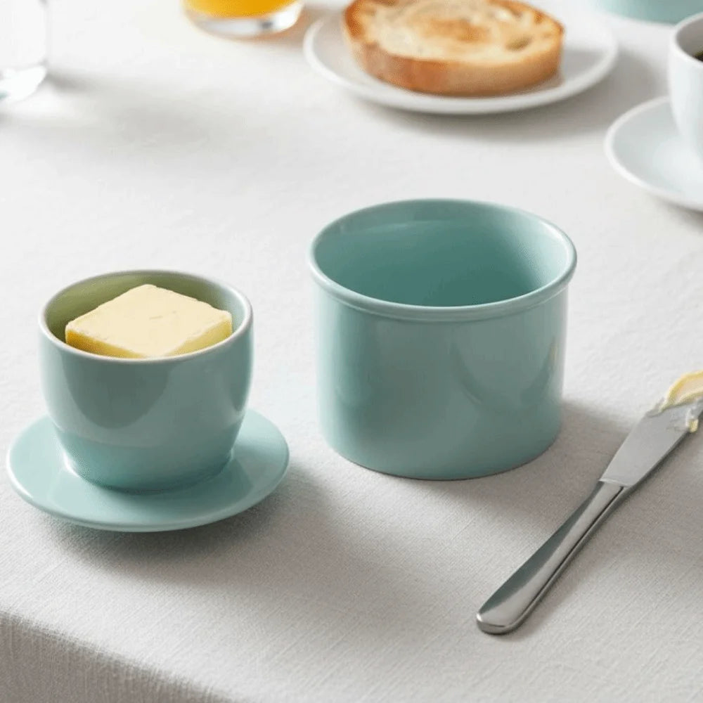 Light blue ceramic French butter crock with lid and cup, shown on a set breakfast table