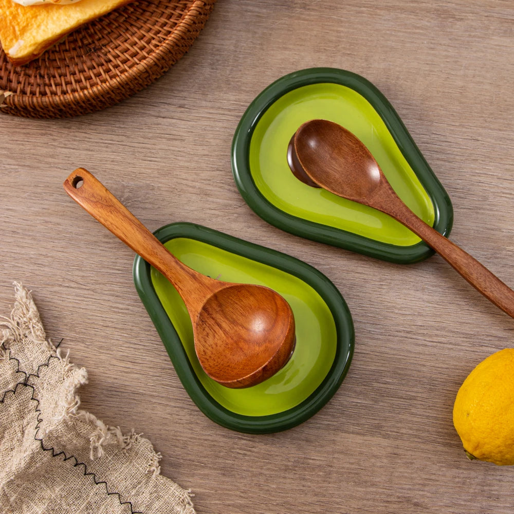 Avocado ceramic spoon rests each holding a wooden spoon on a kitchen countertop