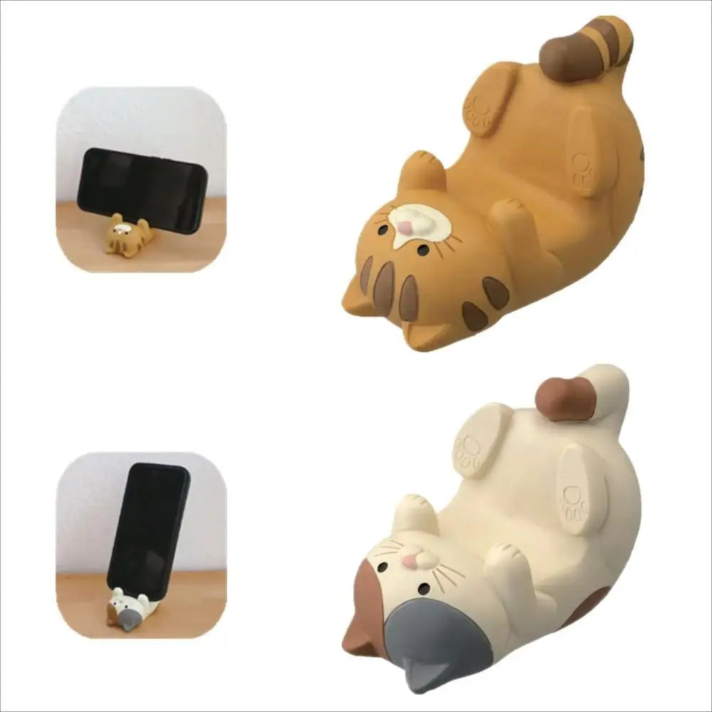 Two cat-shaped resin phone stands in brown and white, each holding a smartphone on a desk