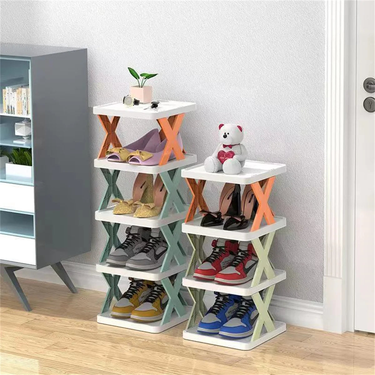 Two shorter multi-layer plastic shoe racks in pastel colors holding shoes, plants and a teddy bear in a bedroom