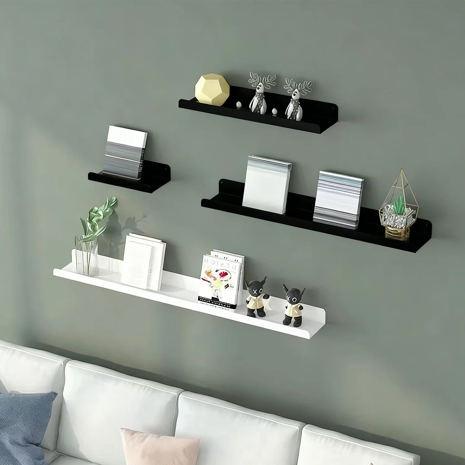 Black and white metal ledge shelves above a sofa on a green wall, decorated with books and ornaments