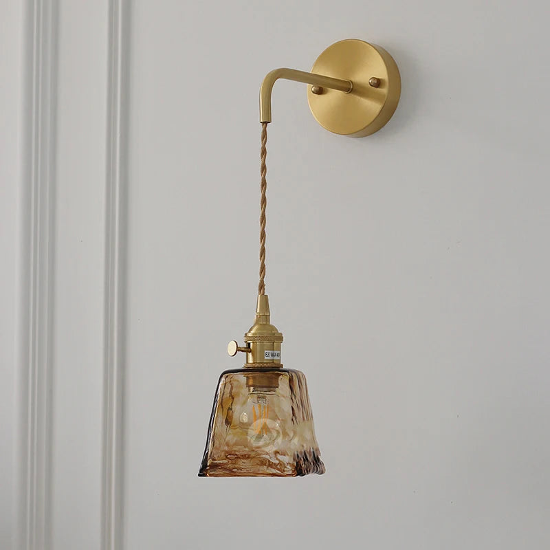 Brass wall-mounted lamp with hanging amber glass shade and twisted cord, side profile