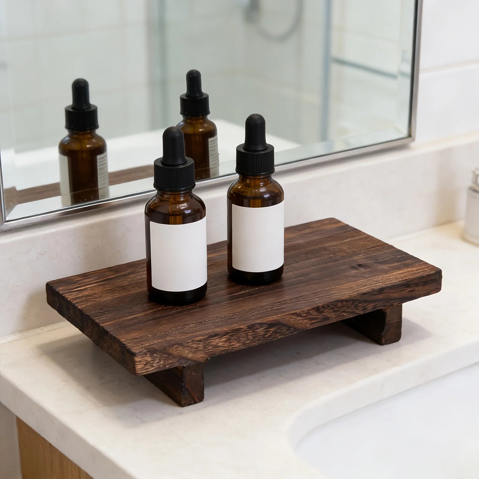Brown wood tray with two dropper bottles in front of a bathroom mirror