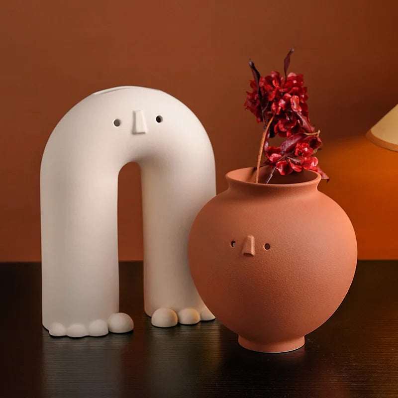 Abstract ceramic face vases, one in white arch shape and one in terracotta round shape, styled on a table